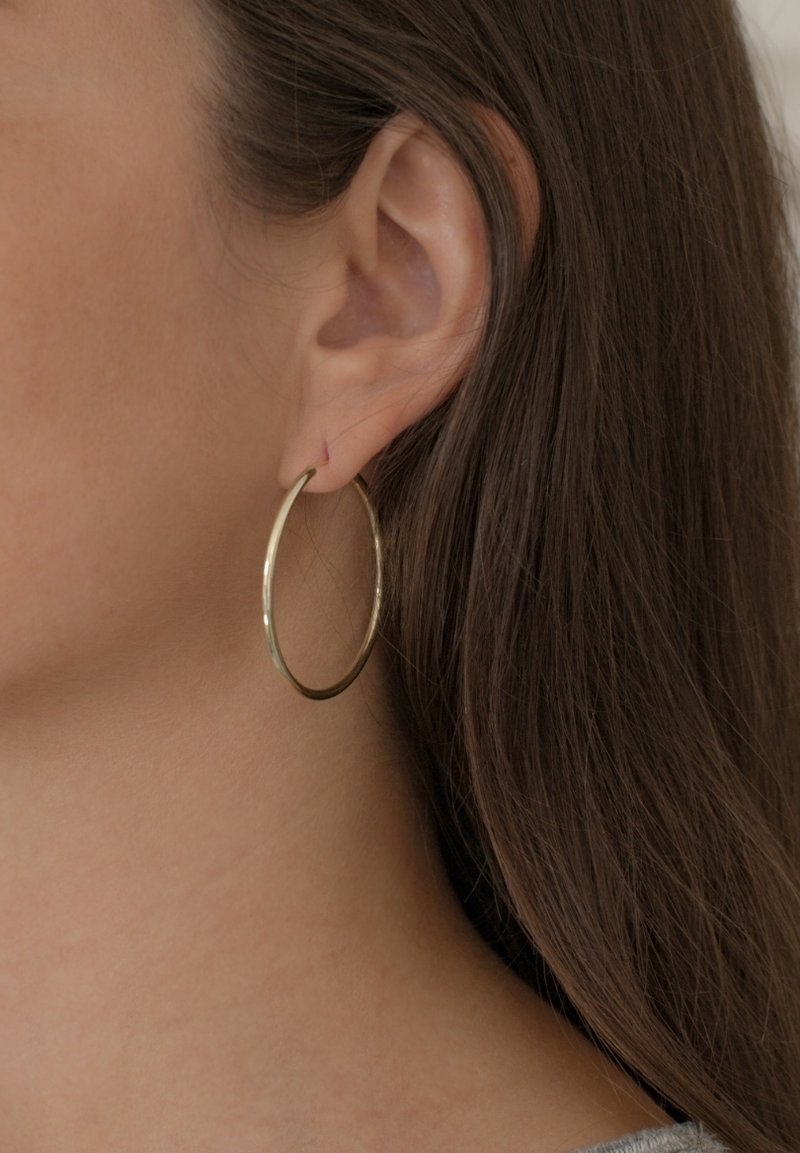 Auksinės auskarai, demonstruojami ant ausies, su lygiu, apvaliu dizainu, plonu profiliu ir blizgiu paviršiumi.