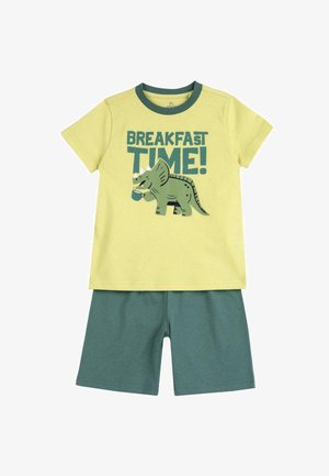 T-shirt di cotone gialla con dettagli verdi, caratterizzata da una grafica di un dinosauro e il testo "ORA DI COLAZIONE!", abbinata a pantaloni corti verdi.