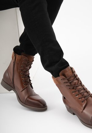 Bruine leren enkelboots met een suède kraag, vetersluiting aan de voorkant en een rits aan de zijkant; platte zool met een lichte hak; gestructureerde afwerking.
