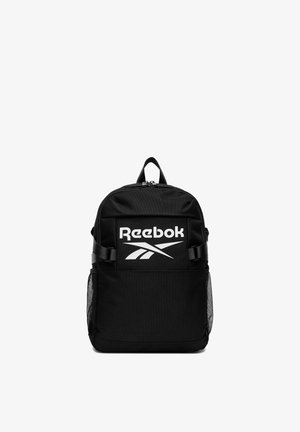 Czarny plecak Reebok z dużym białym logo, przednią kieszenią na zamek, regulowanymi bocznymi paskami oraz siateczkowymi kieszeniami bocznymi, pokazany na białym tle.