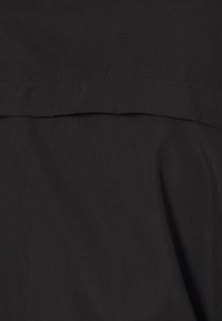 Tela negra con una textura suave, que presenta un diseño simple y un detalle de costura oculta a lo largo de la sección superior.