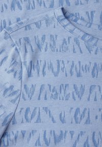 Svetle modré tričko s jemným abstraktním vzorem. Krátké rukávy, kulatý výstřih a měkký textil s hladkým povrchovým úpravou.