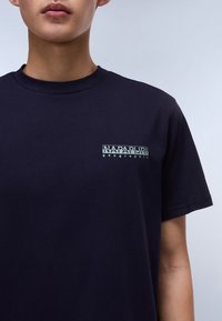 Marineblå bomulds T-shirt med korte ærmer, rund halsudskæring og et lille logo i lysegrøn på venstre bryst med teksten "NAPAPIJRI geographic."