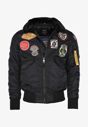 Czarna kurtka bombowca z kołnierzem z sztucznego futra, z zamkiem błyskawicznym i wieloma naszywkami, w tym logotypami i wzorami. Posiada ściągacze przy mankietach i u dołu.