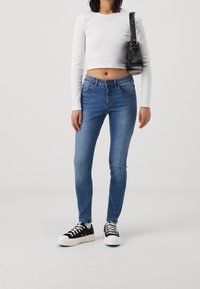 Úzké modré džíny středního odstínu, s pěti kapsami, poutky na opasek a mírným vyblednutím. V páru s bílým crop topem a černými teniskami.