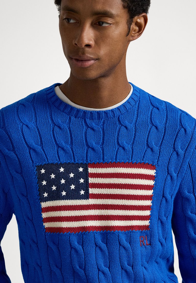 Pull en maille torsadée bleu avec un motif drapeau américain tricoté en rouge, blanc et bleu, avec un détail brodé RL sur l'ourlet.