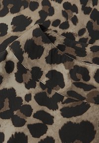 Tkanina w panterkę z dużymi, nieregularnymi czarnymi plamami na beżowym tle. Gładka faktura z detalem w postaci złożonego kołnierza.