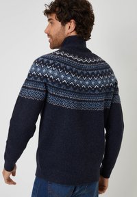 Granatowy sweter dzianinowy z wysokim kołnierzem; posiada geometryczne wzory w jasnoniebieskim i białym kolorze wzdłuż karczku; wykończenie o fakturowanej powierzchni.