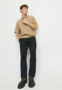 Beige ribbed polo shirt, navy slim-fit trousers, and black loafers. Simple design, short sleeves, smooth texture, and contrasting colors.