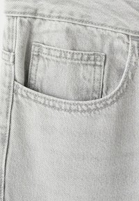 Gros plan sur la poche d'un jean en denim gris clair avec des coutures visibles et un tissu texturé.