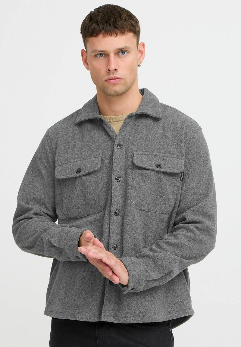 Gray flannel shirt with a button-up front, two chest pockets, and long sleeves. Soft texture and relaxed fit, featuring a collar design.
