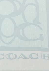 Lyseblåt stof med et geometrisk mønster af sammenlåste cirkler. "COACH" logoet er broderet nederst i en mørkere blå farve. Struktureret vævning.