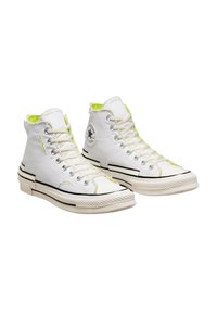 Bílé plátěné sneakers s vysokým střihem, černými akcenty, neonově zeleným podšitím, potrhaným límcem a kulatou nášivkou loga na vnější straně.