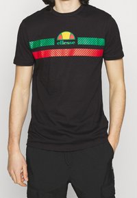 Camiseta de algodón negra con acentos horizontales en verde, rojo y rayas. Logo de Ellesse en un diseño circular encima de las rayas.