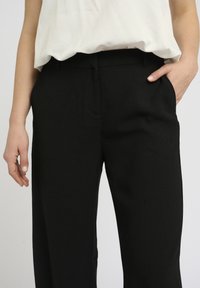 Zwarte op maat gemaakte broek met een gladde textuur, een recht model en zijzakken. Draag een losse witte top erbij.