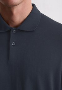 Dunkelblaues Poloshirt aus weichem Material, mit klassischem Kragen, einer Dreiknopfleiste und einer glatten, strukturierten Oberfläche.