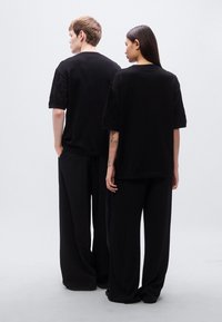 Μαύρα T-shirts με υφασμένα κοντά μανίκια, σε συνδυασμό με φαρδιά μαύρα παντελόνια. Απλός σχεδιασμός και μονοχρωματική χρωματική παλέτα.