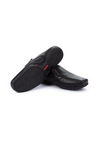 Zapatos de cuero negro con acabado suave, puntera redondeada y costuras decorativas. Suelas de goma con detalle de tracción estampado. Acento rojo en el tacón.