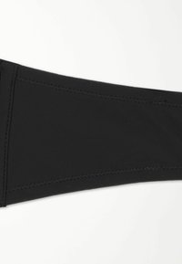 Černý elastický textilní oděv s plochými švy a hladkou texturou, který má ostré linie. Žádné viditelné vzory nebo kovové prvky.