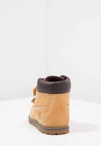 Bottine en cuir marron avec un col en cuir doux marron, des accents en daim et une semelle texturée ; présente des coutures prononcées et un logo de marque.