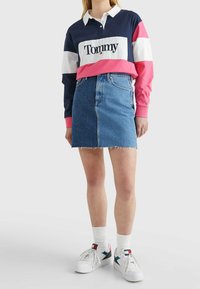 Navy- und pinkfarbener, color-blocked Langarmpolo mit weißem Kragen, kombiniert mit einem blauen Denim-Minirock und weißen Sneakern mit Logoprints.