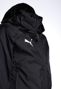 Black lightweight jacket with a zip front, adjustable hood, and a white Puma logo on the left chest. Smooth, water-resistant fabric.