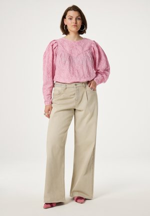 Roze gestructureerde blouse met puffmouwen, gecombineerd met beige wijde broek en roze hoge hakken. Eenvoudige achtergrond, focus op de details van de outfit.