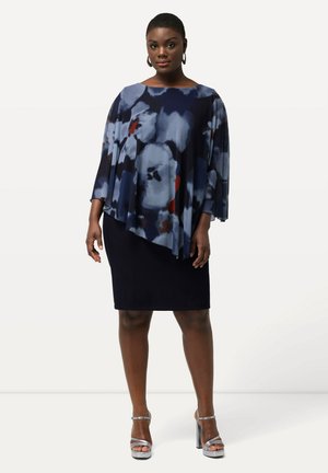 Robe marine avec un dessus fluide à motifs comportant des designs floraux bleus, blancs et rouges ; manches courtes et ourlet asymétrique. Talons argentés.