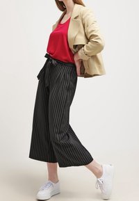 Beige cropped jakke, rød satin tanktop, sort stribet brede bukser og hvide sneakers. Outfittet har en afslappet silhuet og et casual design.