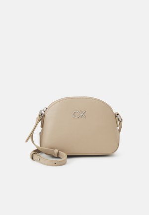 Sac bandoulière en cuir beige avec sangle réglable et logo CK argenté sur le devant, fermeture éclair sur le dessus.