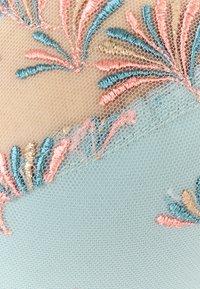 La dentelle brodée en bleu doux arbore des motifs floraux en fils roses et teal, avec une texture transparente et des détails fins le long des bords.