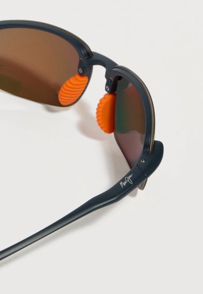 Γυαλιά ηλίου με σκουρόχρωμο πλαίσιο, καφέ φακούς και πορτοκαλί ανάγλυφες μύτες, εμφανιζόμενα σε κοντινή λήψη με φόντο λευκό.