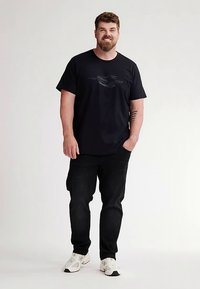 Musta puuvillainen t-paita, jossa graafinen painatus, yhdistetty tummiin farkkuihin ja valkoisiin tennareihin. Painotus rentoon istuvuuteen ja yksinkertaisiin muotoiluelementteihin.