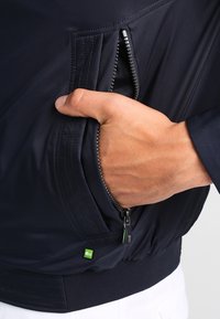Námořnická bunda na zip s texturovanou látkou, postranními kapsami na zip a zelenou značkovou visačkou na dolním lemu.