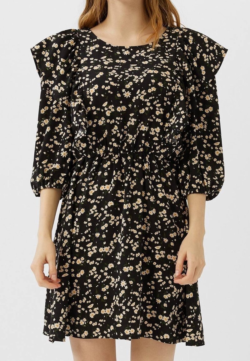 Robe fleurie noire en tissu léger, avec un col rond, des manches bouffantes, une taille élastique et de petits motifs floraux blancs et jaunes.