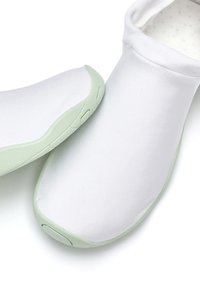 Chaussures slip-on en tissu blanc avec une texture lisse, dotées d'une semelle en caoutchouc vert clair ; forme arrondie avec des détails de design minimalistes.