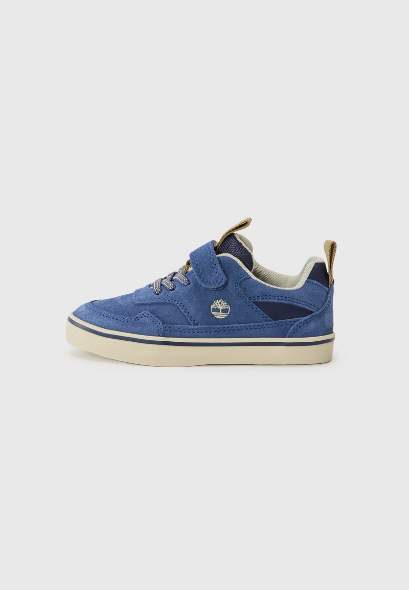 Baskets en daim bleu avec une languette beige, dotées d'une bande Velcro, de lacets et d'une semelle en caoutchouc blanc avec une rayure bleue. Logo Timberland présent.