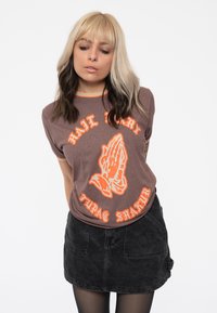 Brown graphic t-shirt with orange text reading "HAIL MARY" and a praying hands design. Screen-printed design, relaxed fit, short sleeves.