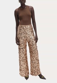 Brun udenærmet top parret med vidde bukser med pailetter i guldtoner. Højkontrast sorte spidse sko med metalliske accenter.