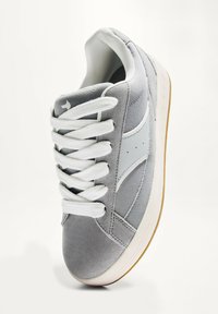 Sneaker grigio con lacci e linguetta bianchi, realizzato con materiali lisci e testurizzati. Accentuato da un logo swoosh grigio chiaro e suola in gomma.