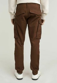 Bruine cargobroek gemaakt van stevig materiaal. Kenmerken zijn twee grote zijzakken en een klassieke pasvorm. Gemaakt met witte sneakers.