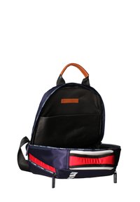 Zaino blu navy con manico in pelle marrone, dotato di un compartimento frontale con cerniera, interno nero e striscia di accentuazione rossa.