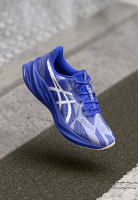 Blue athletic shoe with a textured mesh upper featuring white accents. Rounded toe, cushioned sole, and a dynamic, patterned design.