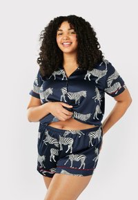 Navy satin pyjamaset med vita zebramönster. Topp med kort ärm och krage samt shorts med elastisk midja, accentuerad med röda detaljer.