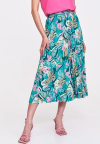 Plisowana spódnica midi w kolorze teal z tropikalnym wzorem liści w odcieniach różu, zieleni i beżu. Połączona z różowymi szpilkami na kostce.