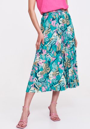 Plisowana spódnica midi w kolorze teal z tropikalnym wzorem liści w odcieniach różu, zieleni i beżu. Połączona z różowymi szpilkami na kostce.