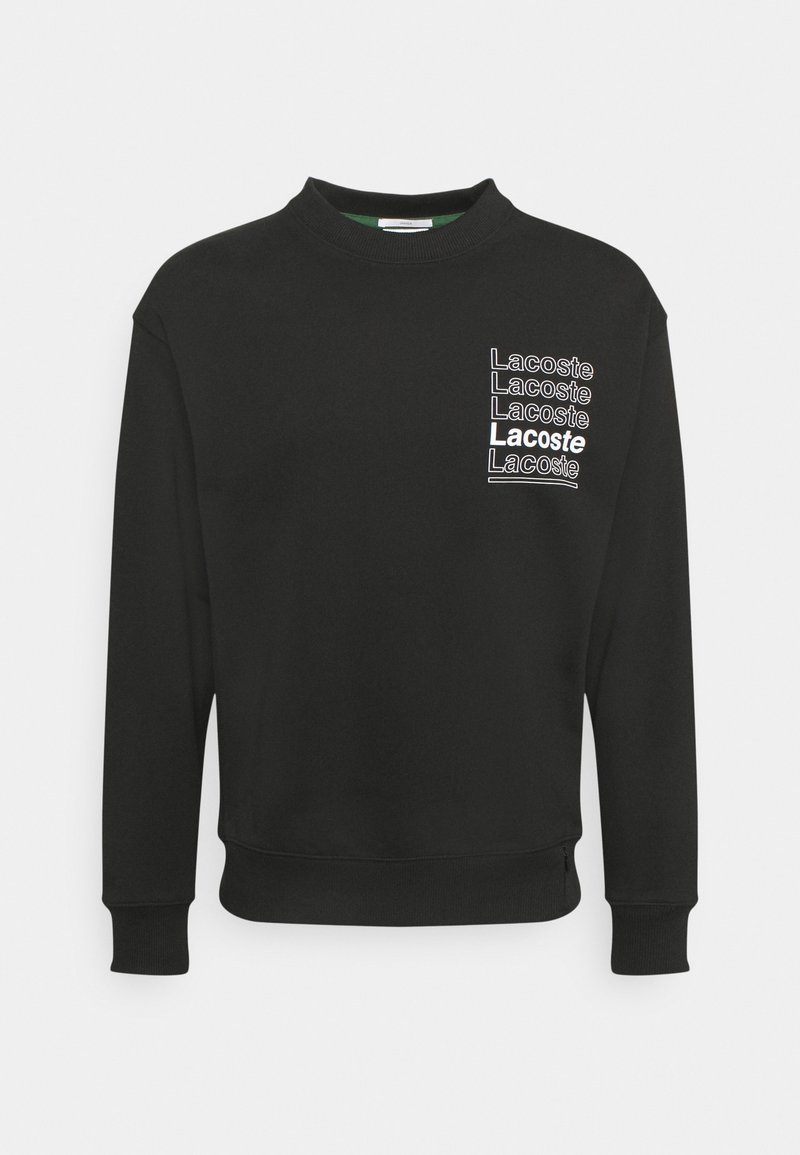 Sweat-shirt noir à manches longues avec col rond et texte blanc "Lacoste" répété sur la poitrine gauche, dont un en gras et souligné.