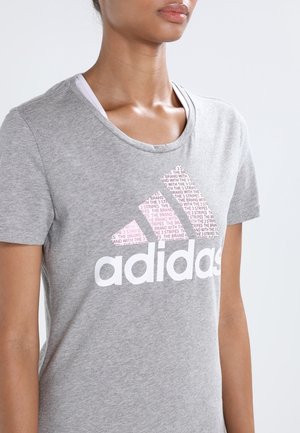 Grå kortærmet t-shirt lavet af bomuld, med et stort hvidt Adidas-logo og et tonalt pink mønster i det ikoniske tre-stribe design.
