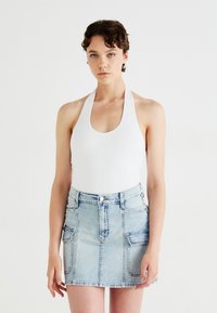 Body alb cu guler halter, asociat cu o fustă mini din denim albastru deschis, dotată cu două buzunare frontale și un fermoar. Textura materialului este netedă.