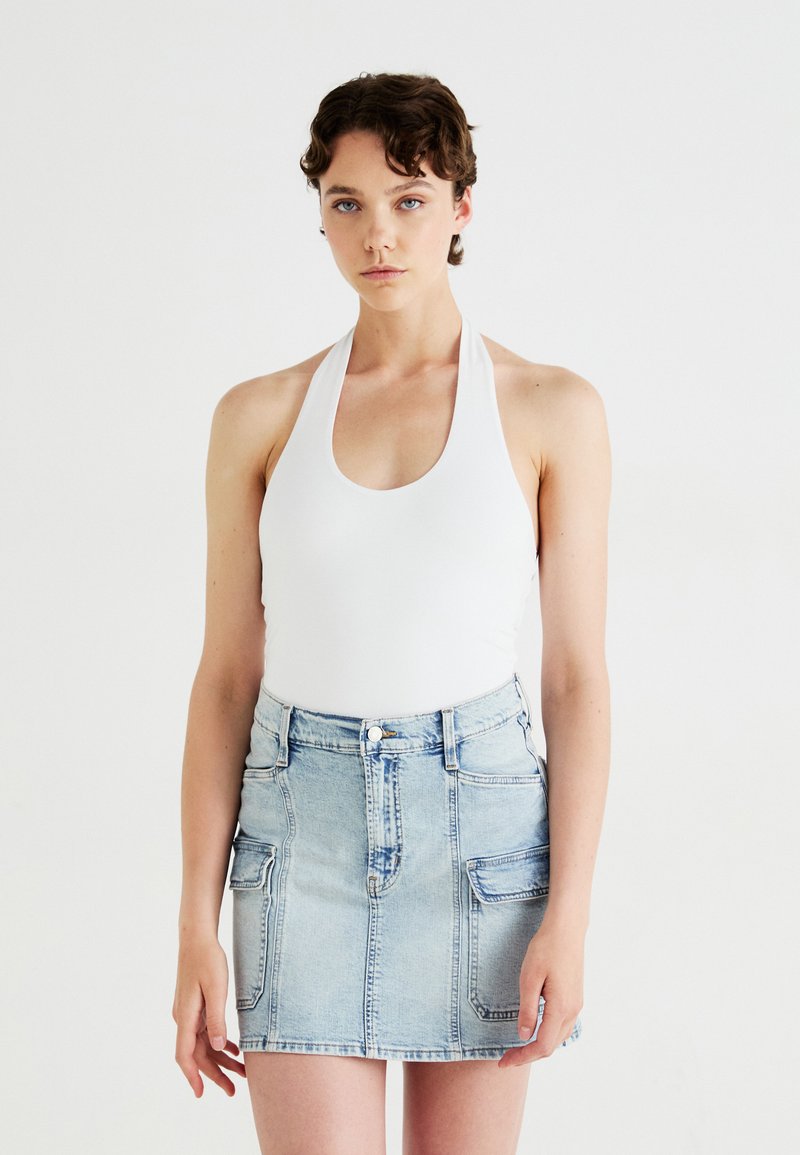 Body alb cu guler halter, asociat cu o fustă mini din denim albastru deschis, dotată cu două buzunare frontale și un fermoar. Textura materialului este netedă.